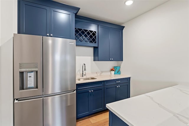 kitchen with light stone counters, sink, stainless steel fridge, and blue cabinetry