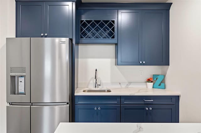 kitchen featuring sink, stainless steel fridge, light stone countertops, and blue cabinets