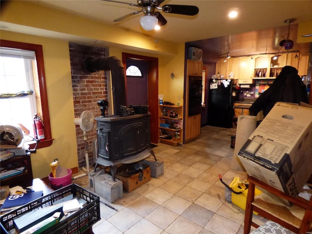 interior space with brick wall, light tile floors, ceiling fan, and a wood stove