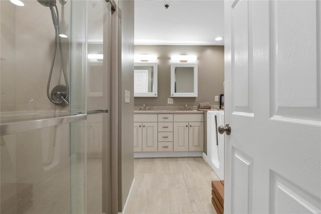 bathroom with a shower with shower door, large vanity, and dual sinks