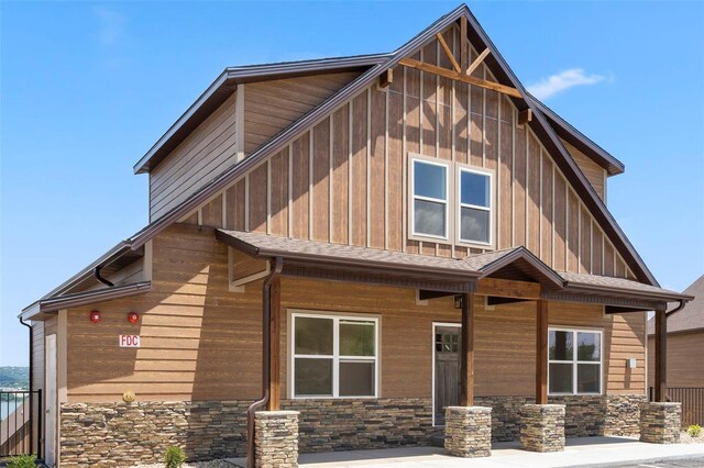 view of front of property with stone siding, a porch, board and batten siding, and roof with shingles