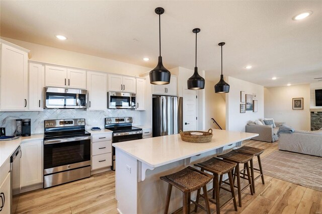 kitchen featuring light countertops, hanging light fixtures, appliances with stainless steel finishes, open floor plan, and white cabinets