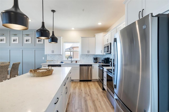 kitchen featuring stainless steel appliances, a sink, white cabinetry, decorative backsplash, and pendant lighting