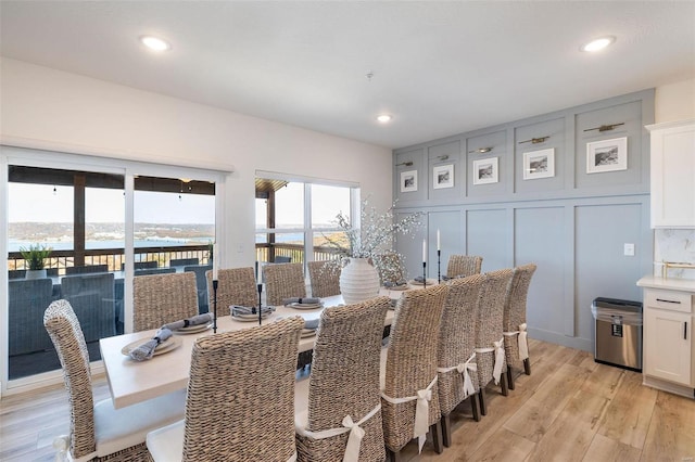 dining area featuring a water view, light wood finished floors, a decorative wall, and recessed lighting