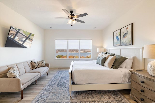 bedroom with a ceiling fan, a water view, and wood finished floors