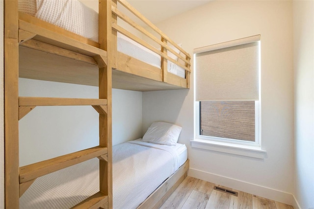 bedroom with light wood finished floors, visible vents, and baseboards