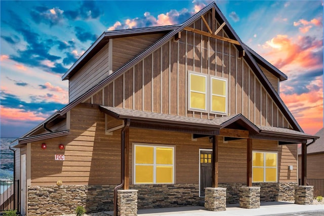 exterior space with stone siding, a shingled roof, board and batten siding, and a porch