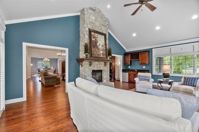 living room featuring dark wood-type flooring, a fireplace, ceiling fan with notable chandelier, high vaulted ceiling, and ornamental molding