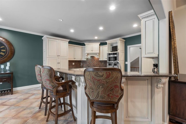 kitchen with backsplash, ornamental molding, dark stone countertops, and a breakfast bar