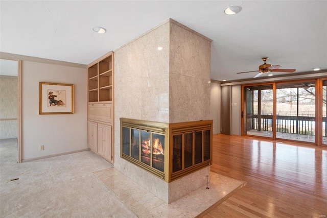 unfurnished living room with a multi sided fireplace, light hardwood / wood-style flooring, and ceiling fan