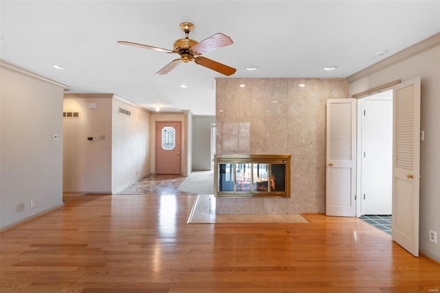 unfurnished living room with light wood-type flooring, a tiled fireplace, and ornamental molding