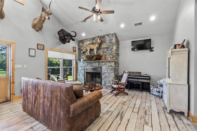 living room featuring a stone fireplace, light hardwood / wood-style floors, ceiling fan, and high vaulted ceiling