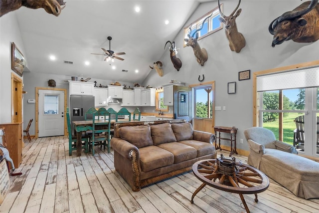 living room featuring a healthy amount of sunlight, light hardwood / wood-style floors, ceiling fan, and high vaulted ceiling