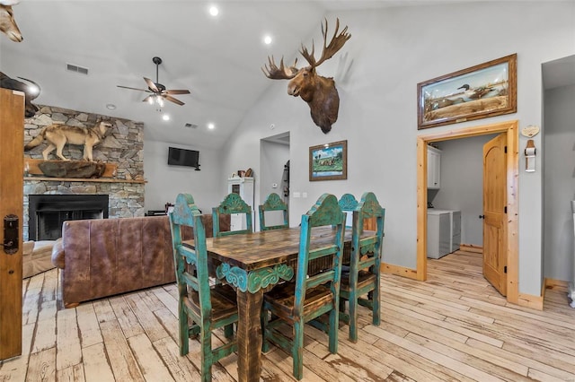 dining space featuring high vaulted ceiling, a stone fireplace, ceiling fan, and light hardwood / wood-style flooring