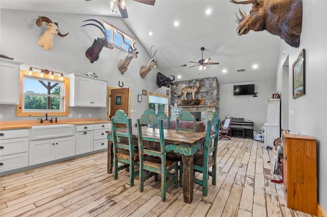 dining room featuring light wood-type flooring, a stone fireplace, and ceiling fan