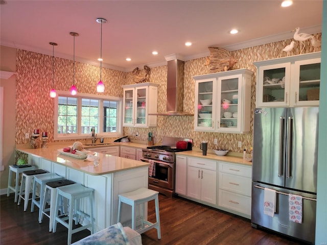 kitchen featuring appliances with stainless steel finishes, hanging light fixtures, wall chimney range hood, a breakfast bar, and white cabinetry