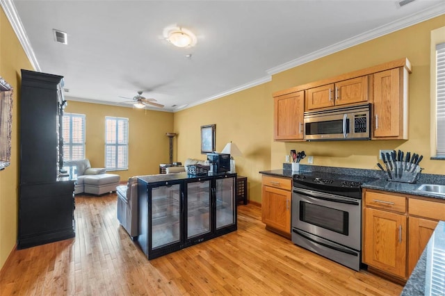 kitchen featuring ceiling fan, dark stone counters, ornamental molding, light hardwood / wood-style flooring, and stainless steel appliances