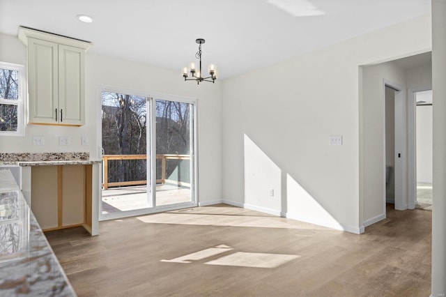 unfurnished dining area featuring an inviting chandelier, plenty of natural light, and light wood-type flooring