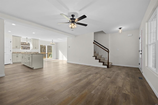 unfurnished living room featuring baseboards, stairs, ceiling fan with notable chandelier, wood finished floors, and a sink