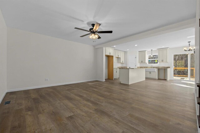 unfurnished living room featuring visible vents, baseboards, dark wood-style floors, and ceiling fan with notable chandelier