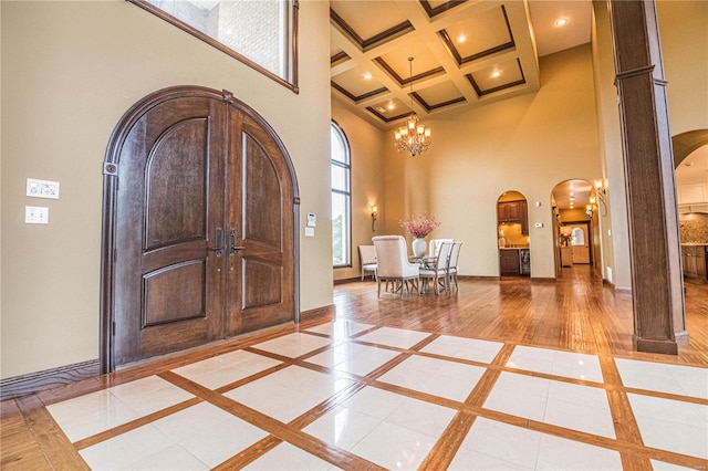 entrance foyer featuring coffered ceiling, a notable chandelier, light wood-type flooring, beam ceiling, and a high ceiling