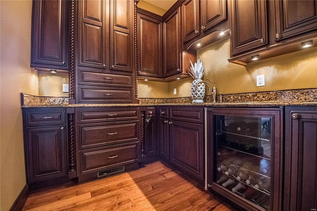 bar featuring dark stone counters, wine cooler, and light hardwood / wood-style floors