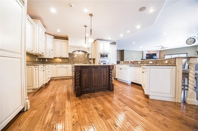 kitchen featuring dark stone counters, ceiling fan, decorative light fixtures, light hardwood / wood-style flooring, and a kitchen island with sink