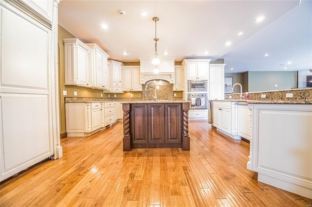 kitchen featuring an island with sink, appliances with stainless steel finishes, light stone countertops, white cabinetry, and light wood-type flooring