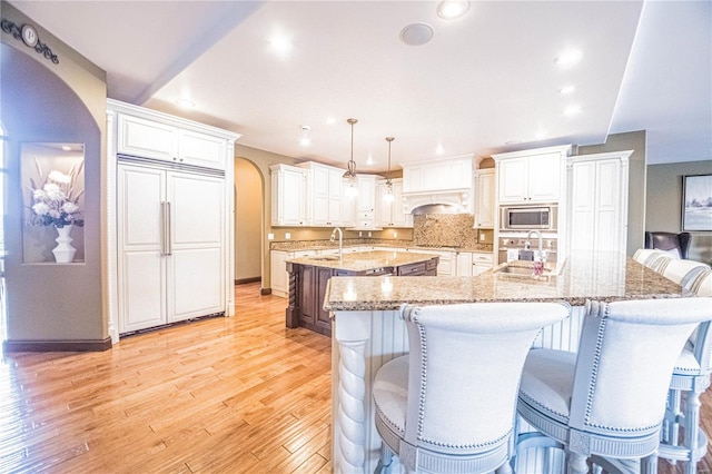 kitchen featuring a kitchen breakfast bar, an island with sink, light hardwood / wood-style flooring, built in appliances, and pendant lighting