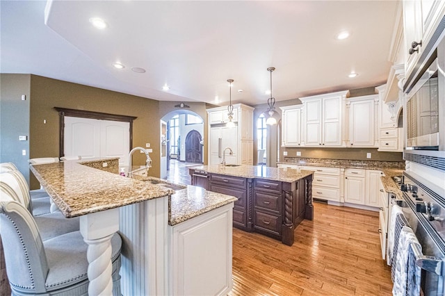 kitchen with an island with sink, sink, a kitchen breakfast bar, light hardwood / wood-style flooring, and light stone countertops