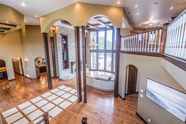 foyer with coffered ceiling, an inviting chandelier, ornate columns, beamed ceiling, and light hardwood / wood-style flooring