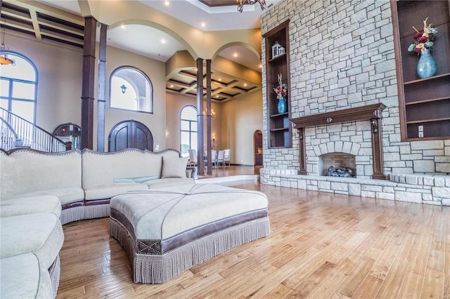 living room featuring coffered ceiling, light wood-type flooring, beam ceiling, a stone fireplace, and ornate columns