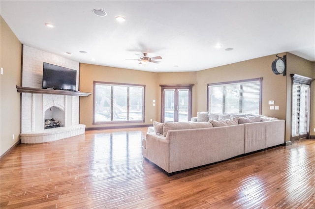 living room featuring ceiling fan, light wood-type flooring, and a brick fireplace