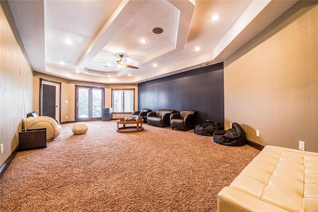 carpeted home theater with ceiling fan and a tray ceiling