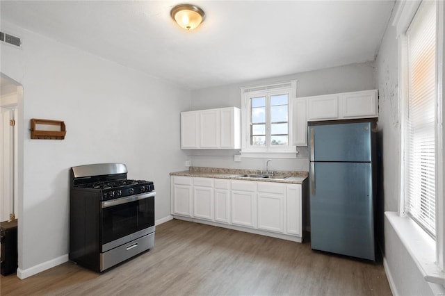 kitchen with light wood-type flooring, appliances with stainless steel finishes, sink, and white cabinets