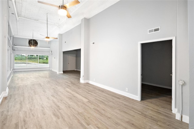 unfurnished living room featuring ceiling fan, a towering ceiling, and wood-type flooring