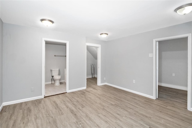 unfurnished bedroom featuring a closet, a spacious closet, ensuite bathroom, and light wood-type flooring