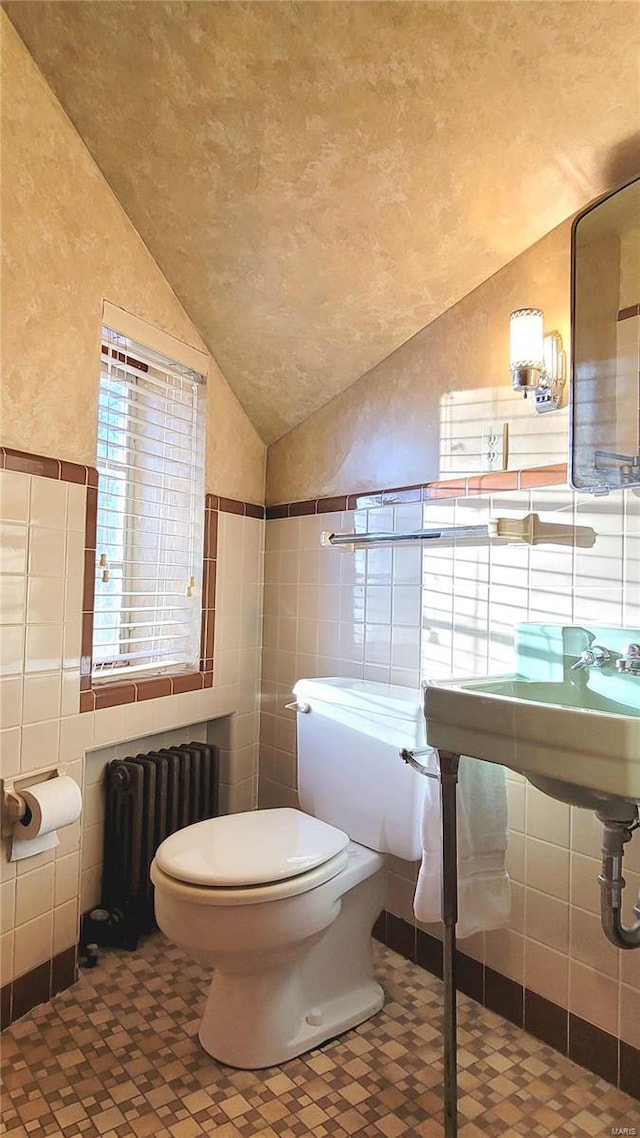 bathroom with vaulted ceiling, radiator, tile walls, and toilet