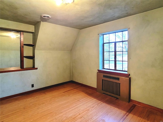 bonus room with radiator heating unit, lofted ceiling, and hardwood / wood-style flooring