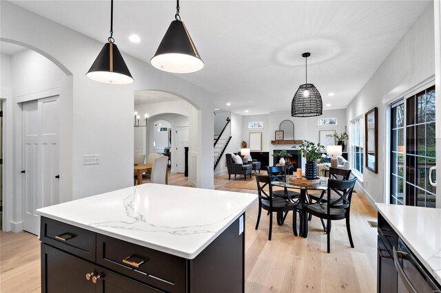 kitchen with light stone countertops, hanging light fixtures, light hardwood / wood-style floors, and a kitchen island