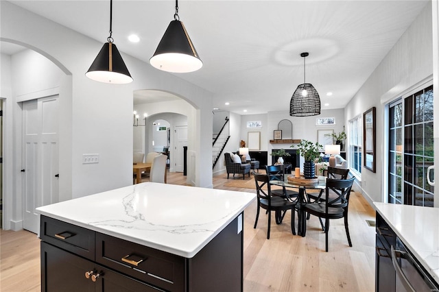 kitchen with decorative light fixtures, a kitchen island, light wood-type flooring, and light stone countertops