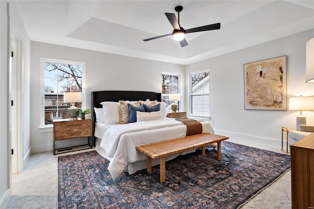 carpeted bedroom featuring multiple windows, a tray ceiling, and ceiling fan