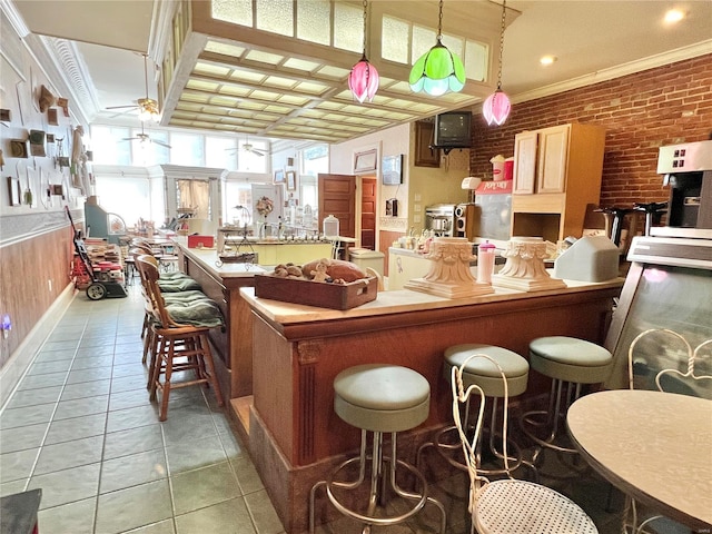 interior space with ceiling fan, tile floors, brick wall, and a breakfast bar