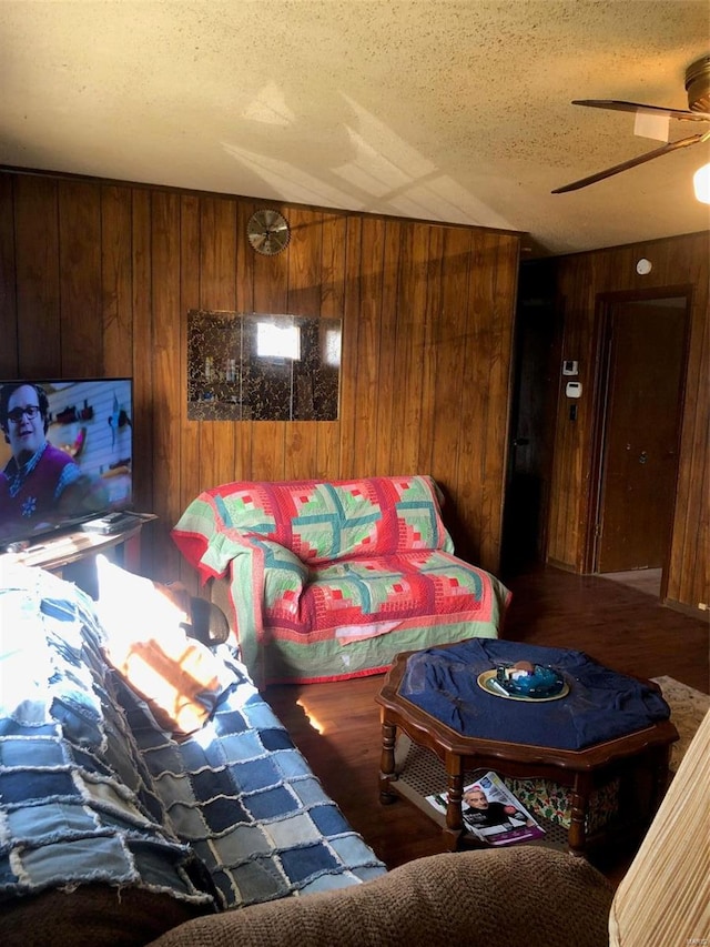 living room with ceiling fan, hardwood / wood-style flooring, a textured ceiling, and wooden walls