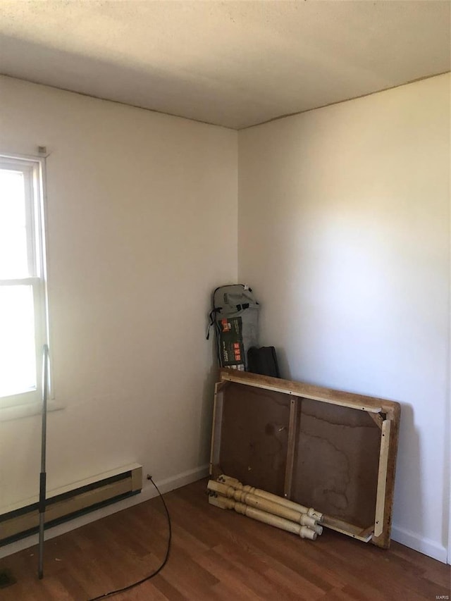 miscellaneous room featuring a baseboard heating unit and dark wood-type flooring