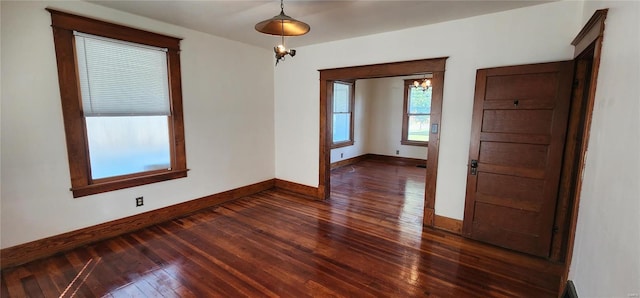 spare room with dark hardwood / wood-style flooring and an inviting chandelier