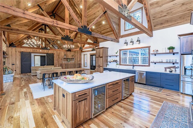 kitchen with light hardwood / wood-style flooring, wine cooler, a center island, stainless steel appliances, and high vaulted ceiling