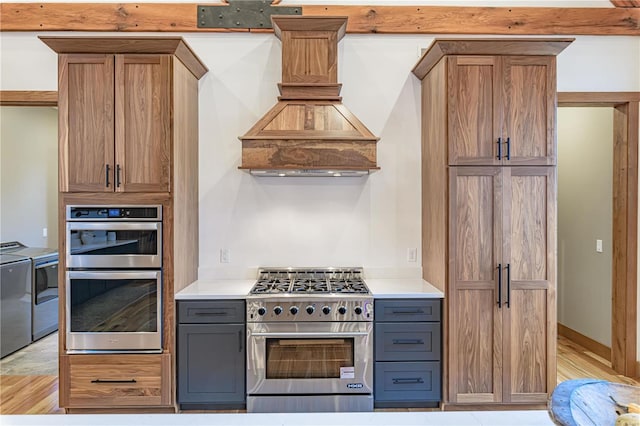 kitchen featuring custom range hood, washing machine and dryer, light hardwood / wood-style flooring, and appliances with stainless steel finishes