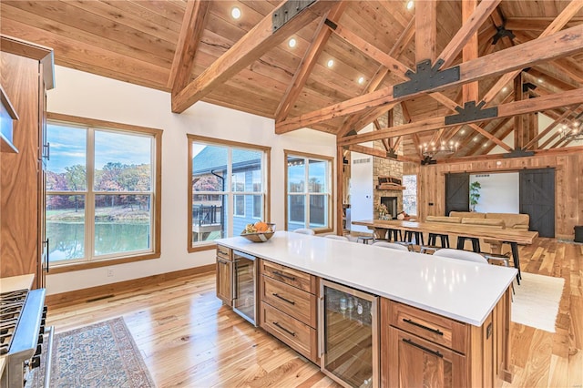 kitchen with a fireplace, light wood-type flooring, beam ceiling, beverage cooler, and wooden ceiling