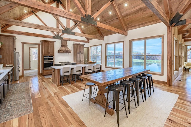 dining area featuring high vaulted ceiling, light wood-type flooring, wooden ceiling, and beam ceiling